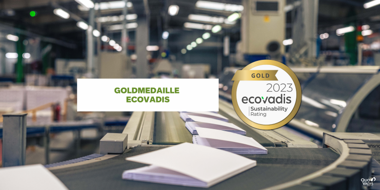 Eine Industrieanlage von Quo Vadis mit einem Förderband, auf dem offene Kalendereinlagen transportiert werden. Der Textüberzug lautet „Goldmedaille EcoVadis“. Ein Logo daneben lautet „Gold 2023 EcoVadis Sustainability Rating“. Im Hintergrund sind Produktionsmaschinen zu sehen.