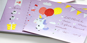 Eine Einladungskarte zum Geburtstag mit einem Einhorn, das rote und gelbe Luftballons hält, vor einem violetten Hintergrund. Details wie eine Geschenkbox, Wolken und ein gelbes Banner schmücken die Karte mit handgeschriebenem Text und einem Datum.