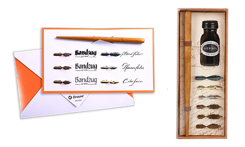 Rechts ein Kalligraphie-Set mit einem Federhalter aus Holz, mehreren Federn und einem Tintenfass von Jacques Herbin. Auf der linken Seite ist eine Karte mit der Aufschrift „Bandzug“ zu sehen, auf der verschiedene Bandzugfedern und ein Federhalter aus Holz eingeklemmt sind. Dieses Set ist von Brause.