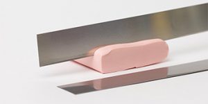Auf einer weißen Oberfläche liegt ein Block rosa Modelliermasse von Cernit, darauf balanciert eine Modellierklinge aus Metall, unter der sich die Reflexionen spiegeln.
