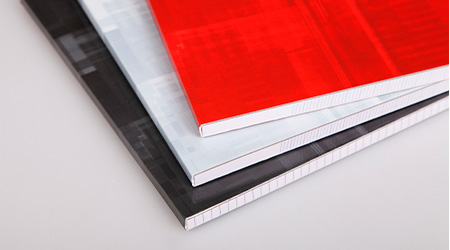 Drei Blöcke von Clairefontaine liegen auf einer glatten, weißen Fläche. Die Einbände haben unterschiedliche Farben: Schwarz, Weiß und Rot, von unten nach oben. Die Blöcke liegen diagonal, mit dem Rücken nach außen.