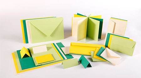 Ausgestellt wird eine Sammlung grüner, gelber und cremefarbener Schreibwaren, darunter Umschläge, Karten und Papier. Die Artikel sind ordentlich und kunstvoll auf einem weißen Hintergrund angeordnet. Es handelt sich um das Korrespondenz-Sortiment von Clairefontaine.