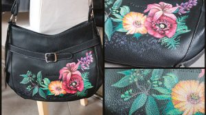 Eine schwarze Lederhandtasche mit Blumenmuster aus rosa, orangefarbenen und gelben Blumen mit grünen Blättern, gemalt mit Ledermalfarbe von Darwi. Die Tasche hat ein Schnallendetail und wird mit Nahaufnahmen gezeigt, die das farbenfrohe Blumenmuster hervorheben.