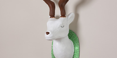 Eine dekorative Wandskulptur eines weißen Hirschkopfes mit geschlossenen Augen und braunem Geweih von Décopatch. Der Hirsch ist auf einer hellgrünen, strukturierten Tafel montiert.