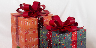 Zwei Geschenkboxen von Décopatch mit großen roten Schleifen. Eine Box ist mit rotem Papier mit weißen Baummustern beklebt, die andere mit grünem Papier mit weinachtlich-festlichem Design. Beide Boxen stehen auf einem weißen Hintergrund.