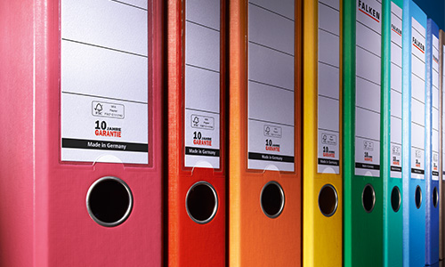 Eine Reihe bunter Ordner von Falken ist ordentlich aufgereiht. Die Ordner sind in den Farben Rosa, Rot, Orange, Gelb, Grün und Blau gehalten. Jeder Ordner hat ein Etikett mit einem runden Griffloch zur einfachen Handhabung.