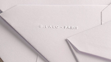 Nahaufnahme mehrerer übereinanderliegender weißer Umschläge mit geprägtem Text „G. Lalo – Paris“ auf einem davon. Die Textur der Umschläge ist leicht glänzend und glatt. Von G. Lalo.