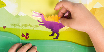 Kinderhände kleben einen lila Dinosaurieraufkleber auf einen bunten Hintergrund mit einem Teich, Bäumen und Bergen. Die Szene ähnelt einer prähistorischen Landschaft mit leuchtenden Farben.