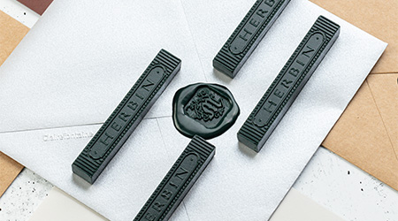4 schwarze Stangen Siegelwachs von Jacques Herbin. Liegend auf perlmuttsilbernen Briefumschlägen von Clairefontaine.