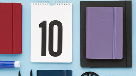 Schülerkalender von Quo Vadis mit rotem und violettem Einband und Spiralkalender mit der Zahl 10 auf hellblauem Hintergrund.