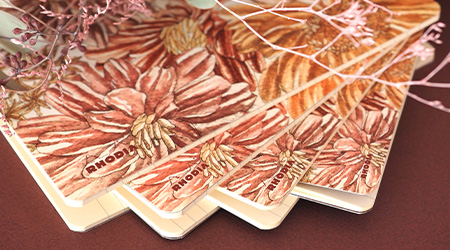 Linierte Notizhefte mit orange-rotem Muster von Rhodia aus der Kollektion Botanik auf bordeauxrotem Hintergrund.