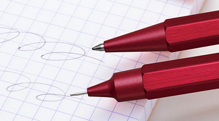 Kulli und Druckbleistift, beide rort, von Rhodia. Auf kariertem Papier liegend.