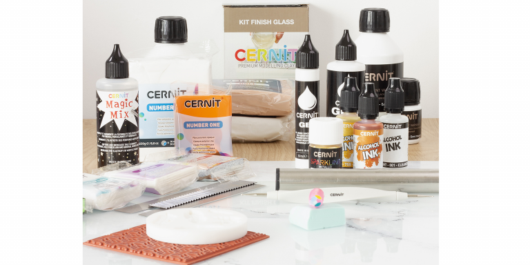 Modelliermasse, Alcoholtinte, Lack, Kleber, Hilfsmittel, Modellierwerkzeug, Epoxidharz und Texturmatte von Cernit auf Tisch präsentiert.