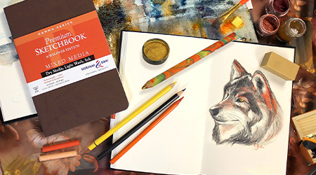 Tisch mit Skizzenbuch Mixed Media Gamma von Stillman&Birn, brauner Einband. Mit Stiften und Pastellkreide. Offenes Skizzenbuch mit Zeichnung eines Huskys.
