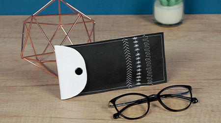 Schwarz-weißes Brillenetui aus Nähpapier von Clairefontaine und schwarze Brille auf Tisch.