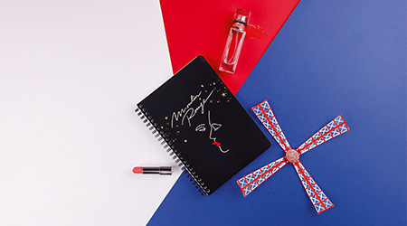 Notizbuch mit Doppelspirale, Lippenstift, Parfum und Rad einer Mühle. Kollektion Moulin Rouge von Clairefontaine.