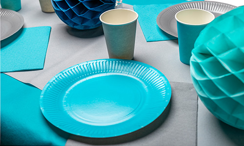 Gedeckter Tisch mit blauen Papptellern- und bechern auf einer grauen Tischdecke.