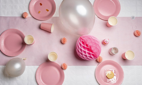Tisch mit rosa Papptellern- und bechern, Luftballons und einem weiß-rosaner Tischdecke.