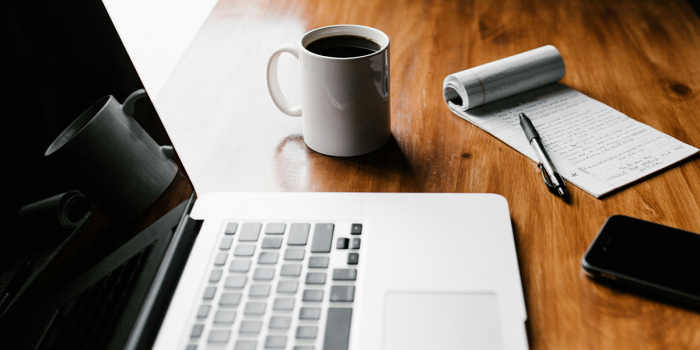 Brauner Holzschreibtisch mit Laptop, Block, Stift, Smartphone und einer Tasse Kaffee.