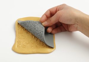 Goldene Texturmatte mit Prägung, von der graue Modelliermasse abgezogen wird. Von Cernit.
