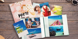 Fotos und aufgeschlagenes Einsteckalbum mit Urlaubsfotos von Exacompta: Lächelndes Paar, Frau mit Sonnenhut am Strand, Kind mit Pusteblume, Taucher im Meer, Frau auf Luftmatratze im Meer.